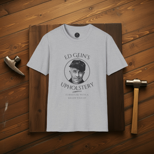 Gray t-shirt with 'Ed Gein's Upholstery' design on a wooden background
